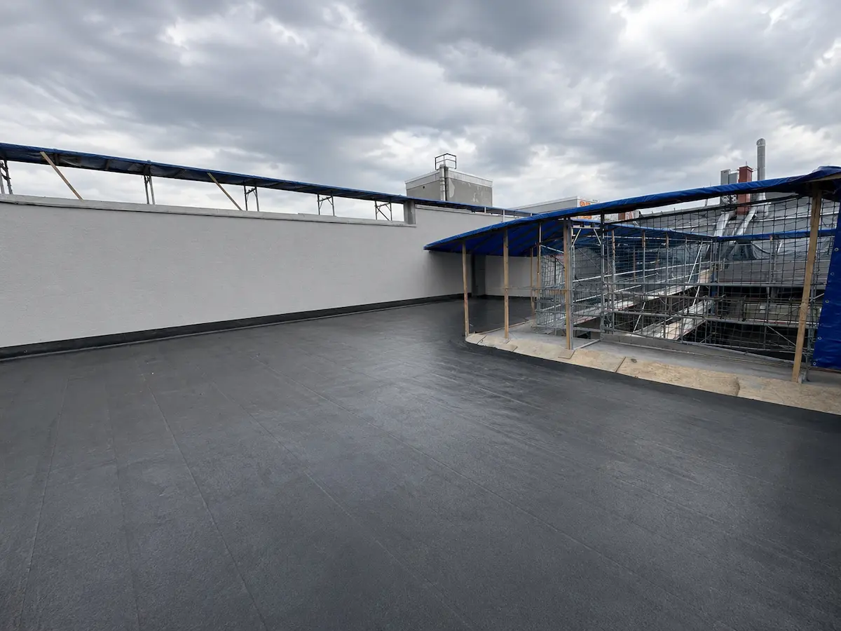 Neue EPDM-Membran auf großer Flachdachfläche mit alter Backsteinmauer im Innenhof, Berlin