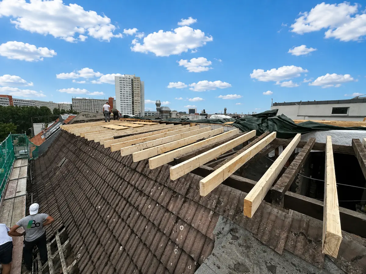 Austausch alter Sparren gegen neue Dachbalken, Arbeiter auf dem Dachfirst mit Stadtblick