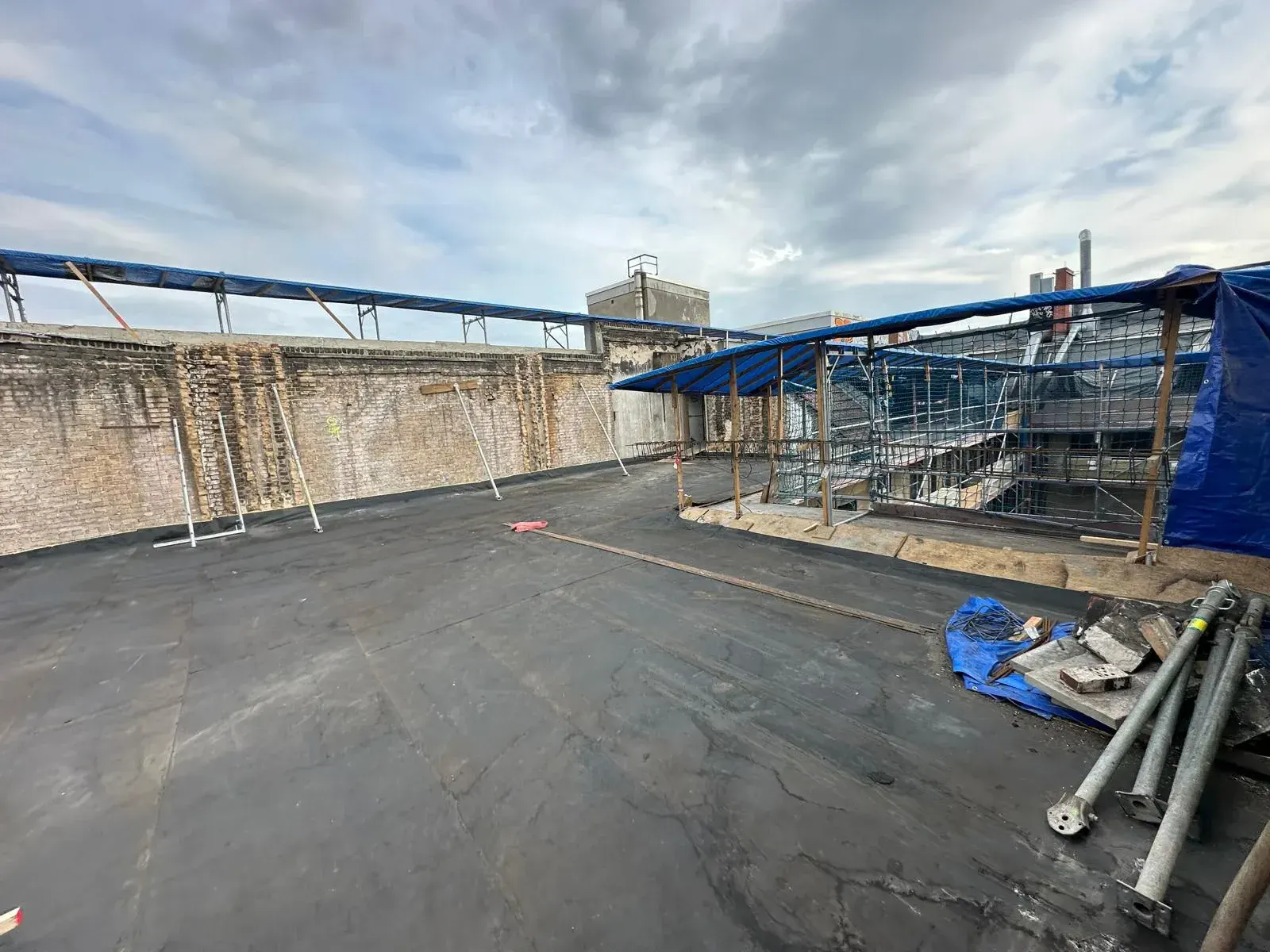Neue EPDM-Membran auf großer Flachdachfläche mit alter Backsteinmauer im Innenhof, Berlin