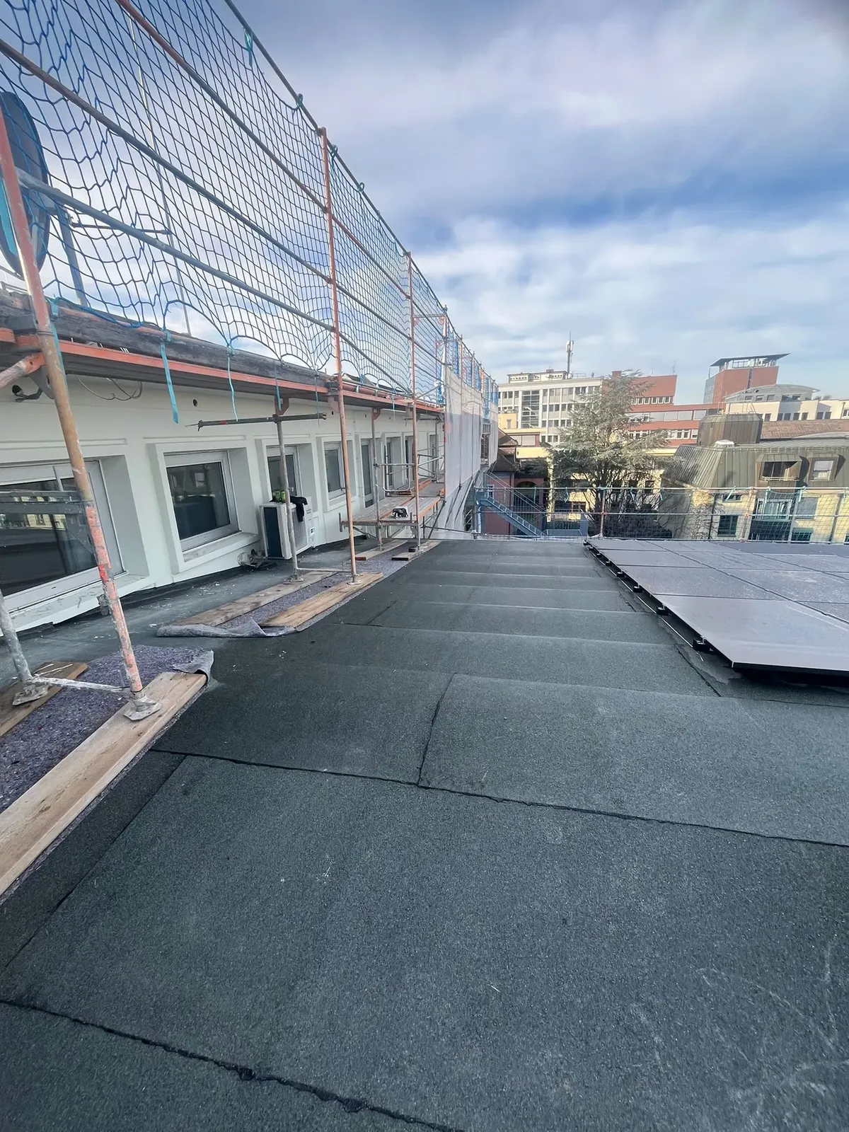 Übersicht eines Flachdachs mit teilweise montierten Solarpanelen, moderne Fassade im Hintergrund