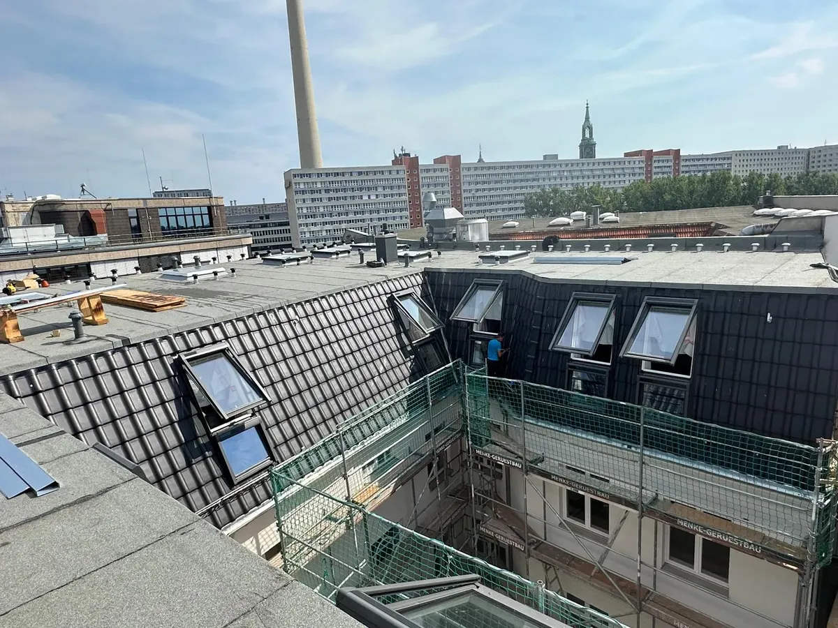 Fertiggestelltes Mansarddach mit anthrazitfarbener Ziegeldeckung, geöffneten VELUX-Fenstern und Blick auf den Fernsehturm