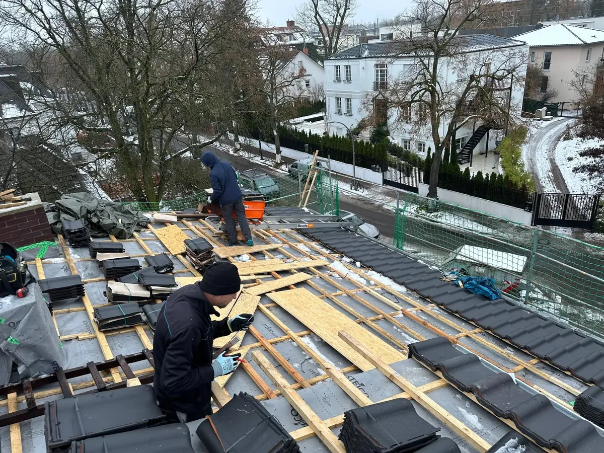 Verlegung anthrazitfarbener Dachsteine auf der Lattung im Winter, Villenviertel im Hintergrund