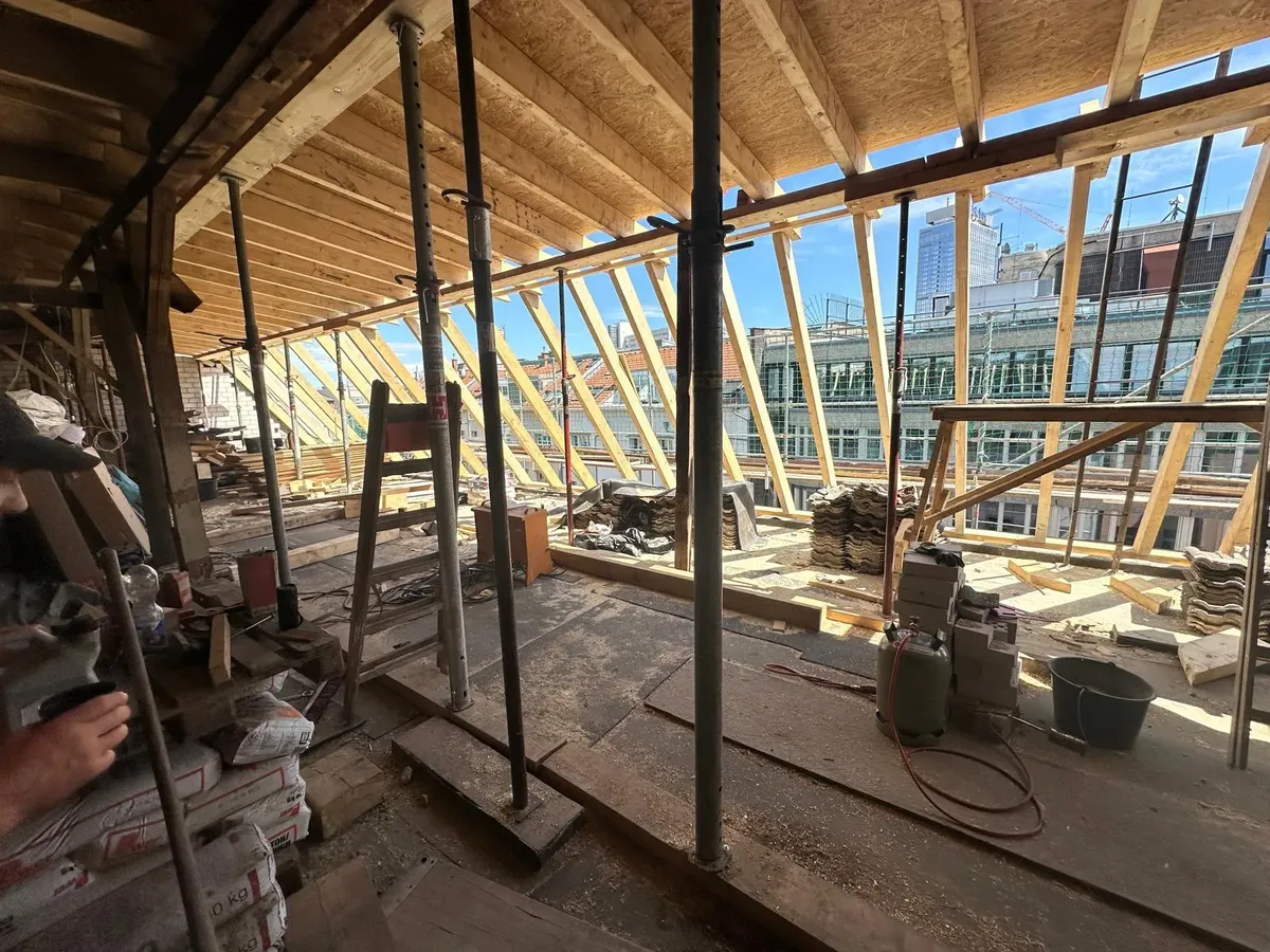 Neue Dachsparren mit bereitgelegten Dachziegeln, Stadtblick mit Baukran im Hintergrund