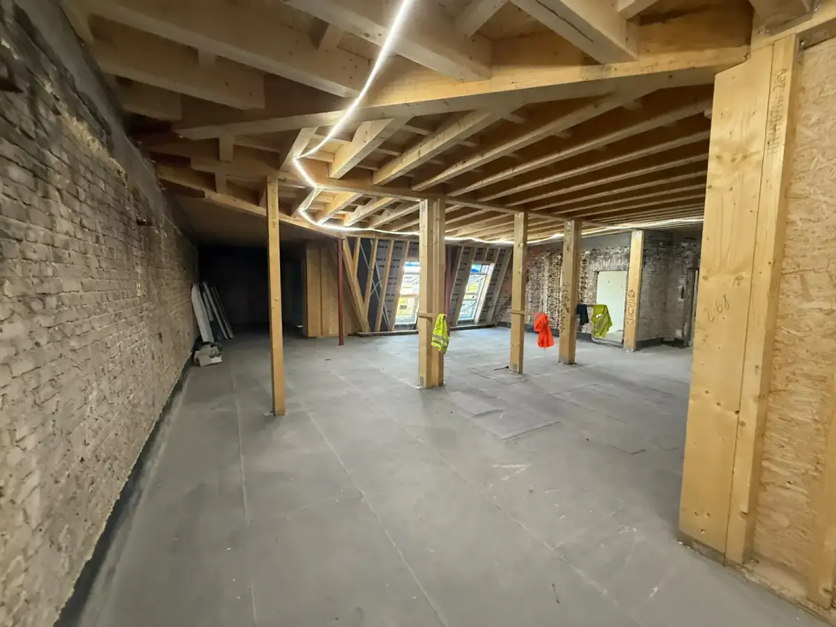 Großzügiger Dachgeschossraum mit Holzstützen und LED-Beleuchtung während der Bauphase