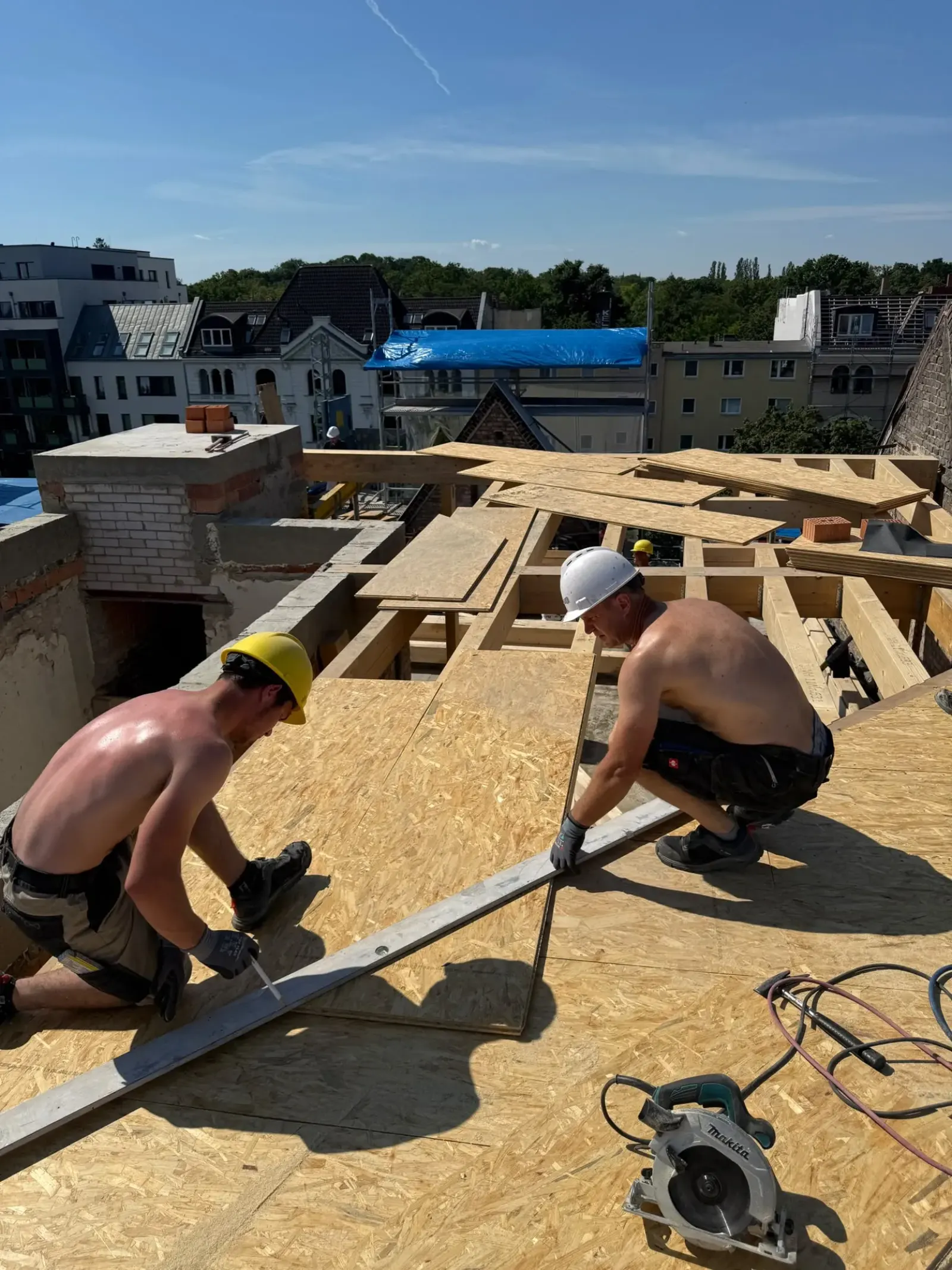 Zwei Arbeiter mit Helmen verlegen OSB-Schalung auf einer neuen Dachstuhlkonstruktion