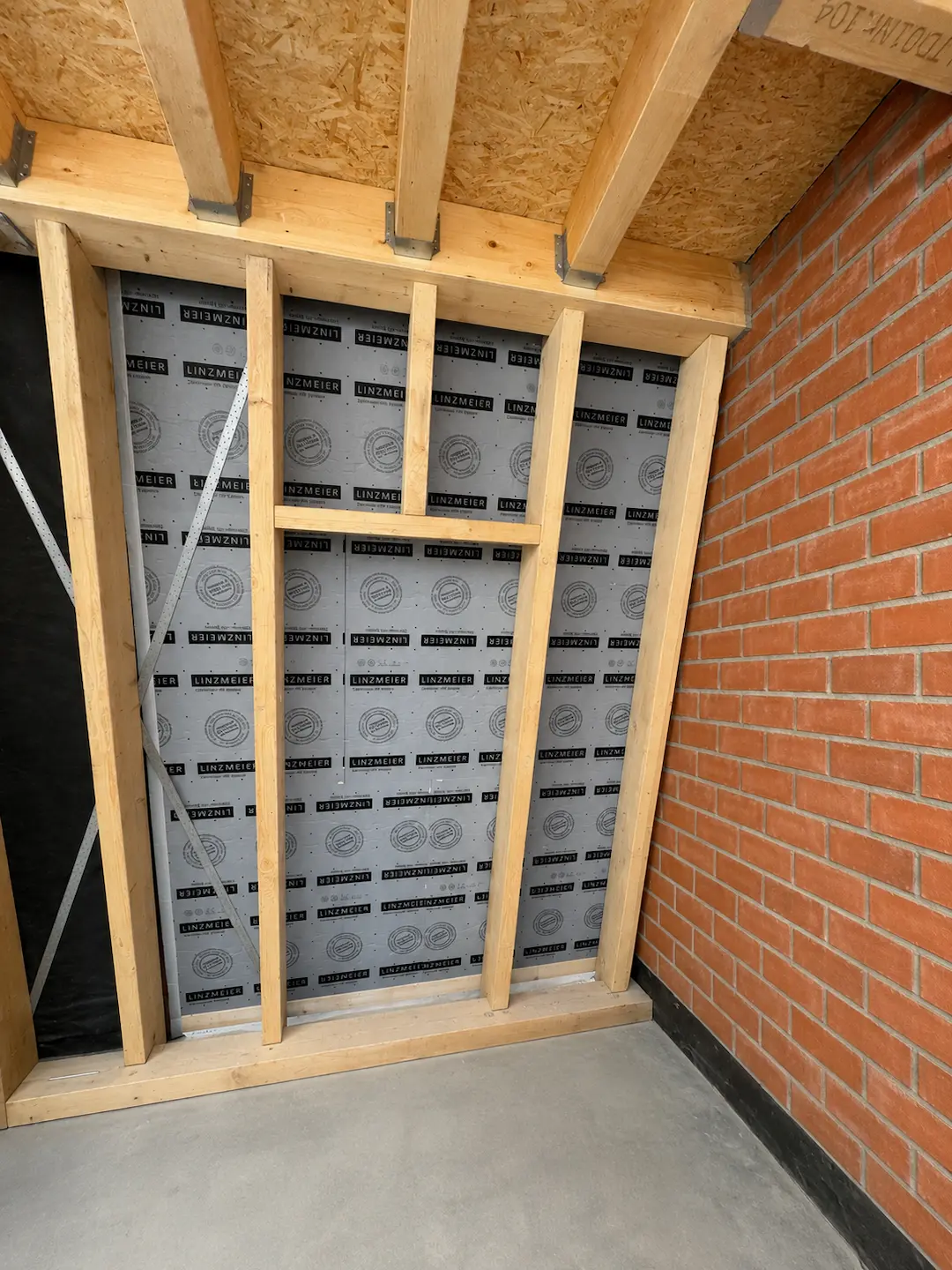 Holzständerwand im Dachgeschossausbau mit moderner Dämmung und gemauerter Ziegelwand während der Sanierungsarbeiten in Berlin.
